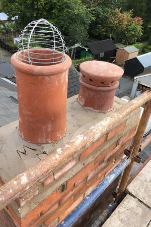 On the left is a wire cowl to discourage nesting birds in summertime, set in a terracotta pot, serving a flue in use.  To the right is a ‘mushroom’ cowl on a terracotta Victorian chimney pot, serving a flue which is no longer in use. 